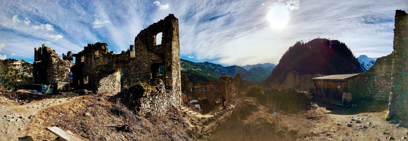 Photo of medieval castle ruins against the Austrian Alps and a cloud-streaked blue sky. 