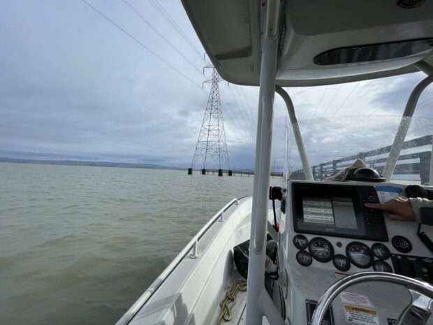 A boat docked in South San Francisco Bay. The boat console is in the foreground and an electrical tower and water and in the background.